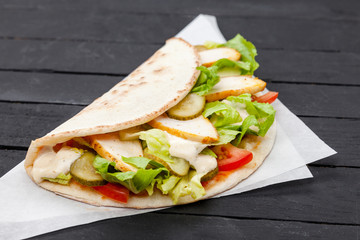 Street food calzone, stromboli wrapped in paper on a black background