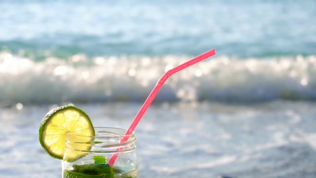 Close up of glass of mojito alcoholic cocktail standing in the sand on a beach