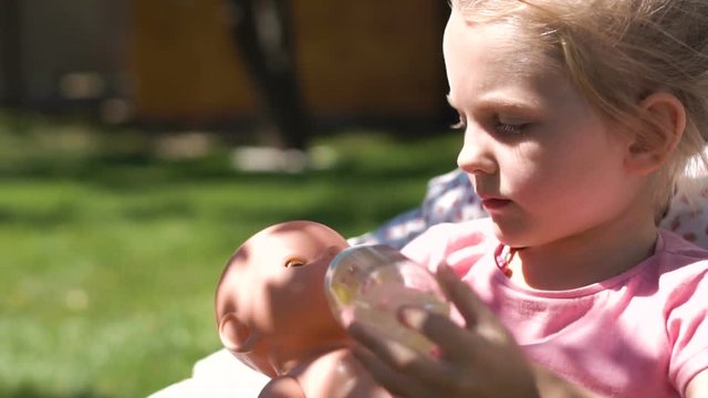 Slow motion of little girl relaxing in armchair in garden playing and feeding baby doll.