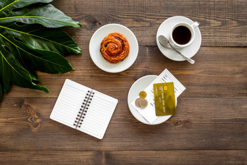 Pay restaurant bill. Bill, bank card, coins near cup of coffee on dark wooden table top view