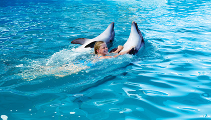Naklejka premium Happy child and dolphins in blue water. Dolphin Assisted Therapy