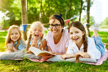 Restful and joyful kids and their teacher spending leisure with book of tales in park