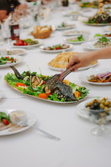 Hand with tongs keeping pieces of fish during banquet.