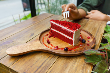 slice of red velvet cake on wooden plate with asian female hand holding fork on wooden table with...