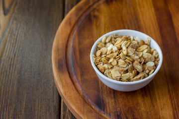 Granola or muesli in white ceramic bowl over wooden table.