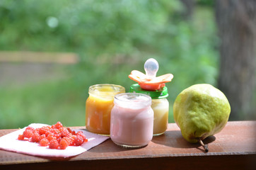 Baby food in jars puree mashed food on a background of foliage, With a pear banana, pacifier and a...