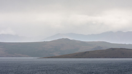 magnificent lake near sandy hill with white fluffy clouds in blue sky
