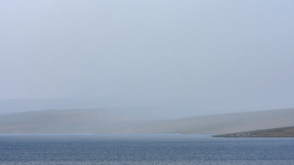 Obraz premium magnificent lake near sandy hill with white fluffy clouds in blue sky 