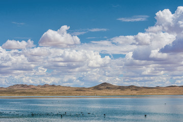 magnificent lake near sandy hill with white fluffy clouds in blue sky
