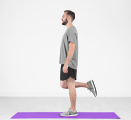 Sporty young man training legs on mat in gym