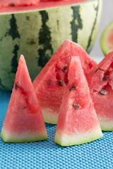 Half a watermelon and slices of watermelon on a blue napkin.