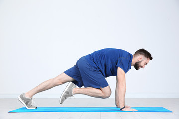 Sporty young man training legs on mat in gym