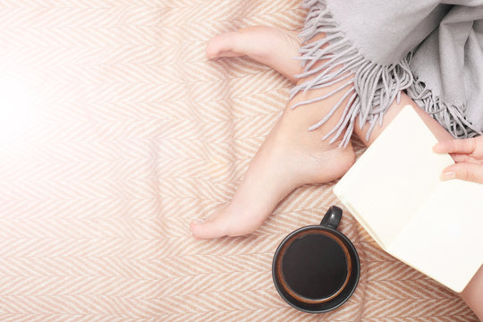 Cozy woman with book and cup of coffee on wooden blanket