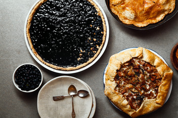 Variety of autumn pies: blueberry tart, chantarelle galette and classical apple pie with sweet pastry crust. Harvest time baking concept. Concrete rustic background.