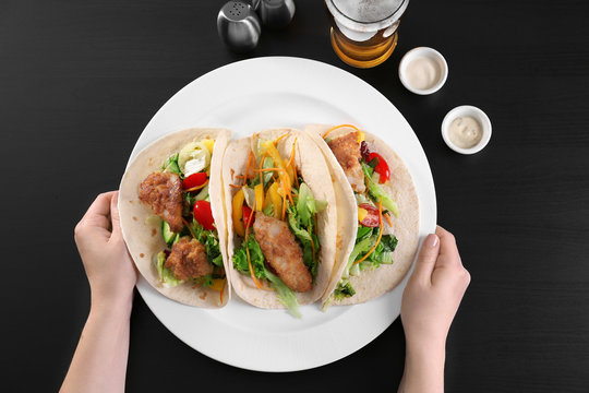 Hands holding plate with delicious fish tacos on black background