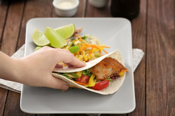 Hand taking delicious fish taco on plate on wooden table