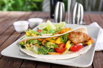 Delicious fish taco served on white plate on wooden table