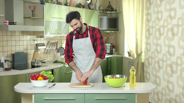 Man cutting apple. Bearded guy in apron, kitchen. Fruit and vegetable salad recipes.