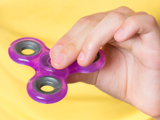 Female child hand holding popular fidget spinner toy - close up. Girl playing with a orange Spinner.