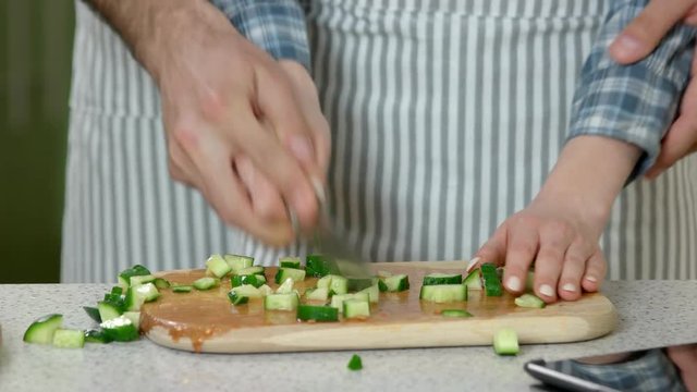 Hands of couple cooking food. Vegetable pieces on wooden board.