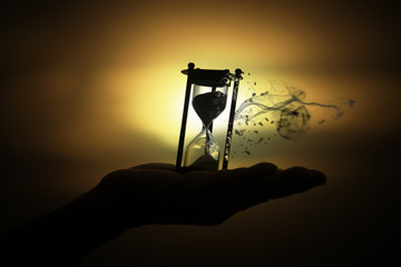 Silhouette hourglass is disintegrating on hand Pocket watch at last sunlight (Concept of wasting...