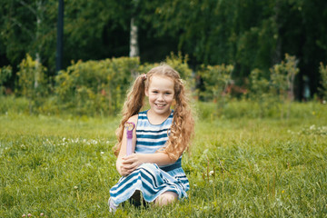 Obraz premium Smiling child girl wearing blue summer dress is playing in park