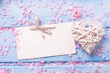 Decorative heart, empty tag and pink petals  on blue wooden background.