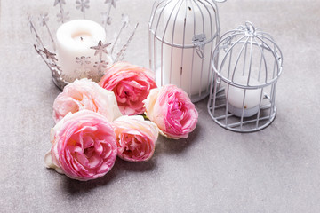 Postcard with fresh pink flowers roses and candles in  candleholders  on grey slate background.