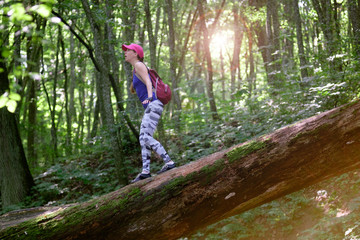 Naklejka na ściany i meble girl hiking in forest, climbing down the log with surprise expression on face