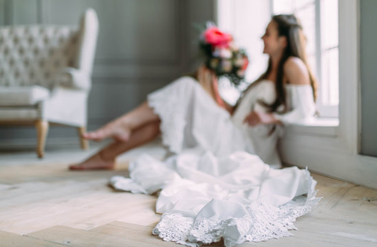 Blurred image of cheerful, young bride which holds a rustic wedding bouquet on panoramic window background. A happy girl with a bunch of flowers, selective focus on the lace of dress
