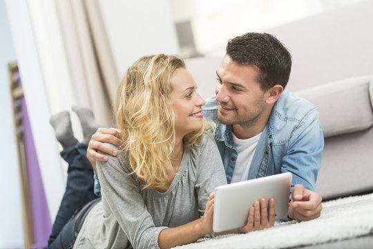 Happy young couple layed on the carpet of their living room and using a tablet