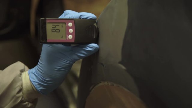 Worker measures a thickness of primer on a car's body using a thickness gauge 4K