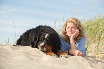 mature woman with her dog on sand and grass lying