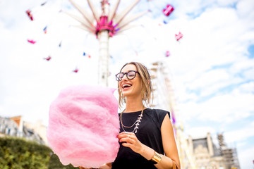 Young woman standing with pink cotton candy in front of the ferris wheel at the amusement park