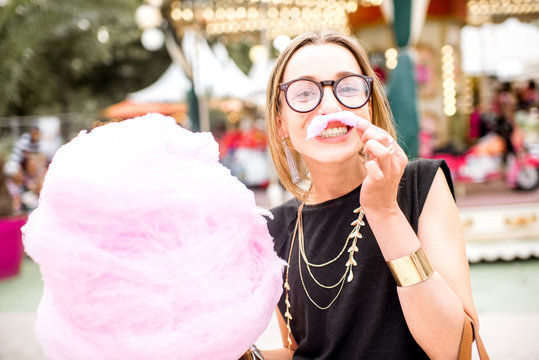 Young woman making mustache with pink cotton candy standing outdoors at the amusement park