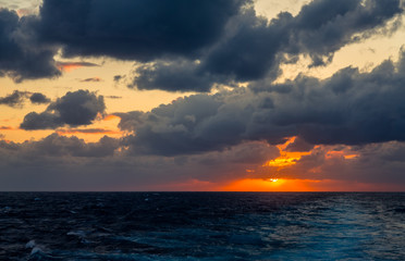 Sunset and dramatic set of clouds drifting over the tropical waters of the Caribbean Sea are lit by the last moments of daylight.