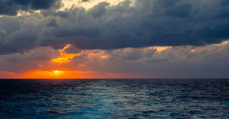 Sunset and dramatic set of clouds drifting over the tropical waters of the Caribbean Sea are lit by the last moments of daylight.