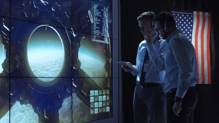 Two employees in headphones in the control center of space flights discuss the flight of the spacecraft to the moon and control its landing.