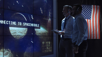 Two employees in headphones in the space flight control center discuss the flight of a spacecraft and establish a video contact with a satellite in space.