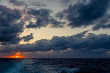 Sunset and dramatic set of clouds drifting over the tropical waters of the Caribbean Sea are lit by the last moments of daylight.