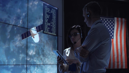 Side view of man and woman communicating in space flight control center. Some elements of this image furnished by NASA.