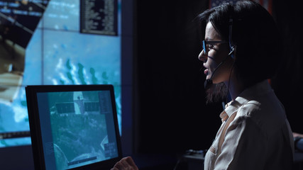 Side view of woman sitting and working at computer in space mission control center. Some elements...