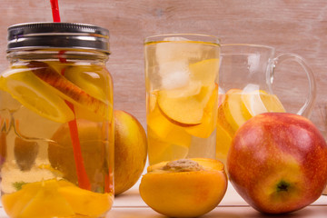 Ice tea with peaches and apples on a rustic wooden background. Detox water from fresh fruit.