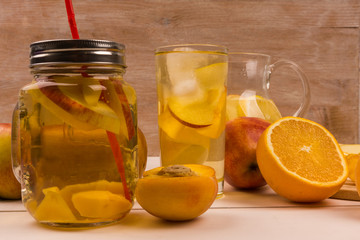 Glasses with detox water with oranges, peaches and apples. Ice tea with fresh fruit on a wooden background
