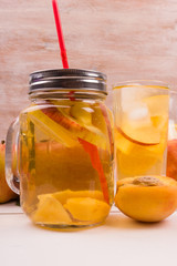 Ice tea with peaches and apples on a rustic wooden background. Detox water from fresh fruit.