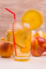Glasses with detox water with oranges, peaches and apples. Ice tea with fresh fruit on a wooden background