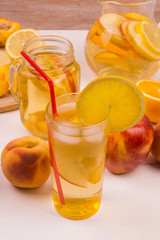 Glasses with detox water with oranges, peaches and apples. Ice tea with fresh fruit on a wooden background