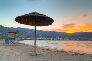 Beach with parasols at Mirabello Bay at sunset, Greece