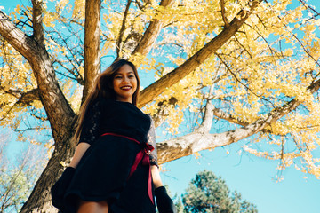 Happy young woman in park on sunny autumn day, smiling. Cheerful beautiful girl in black retro dress autumn fashion style