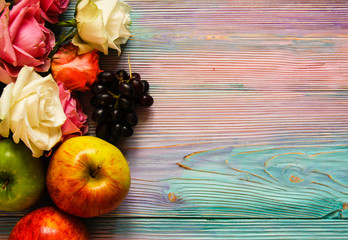 Colorful wooden background with roses, grapes and apples